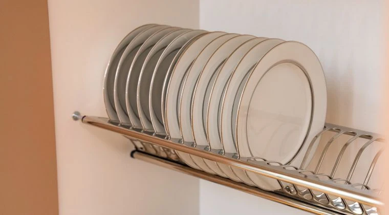 A neatly arranged set of white plates elegantly displayed on a chrome dish rack in a modern kitchen setting