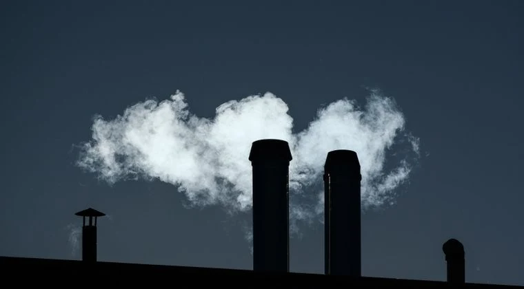 Silhouetted chimneys emit smoke into the sky creating an industrial scene