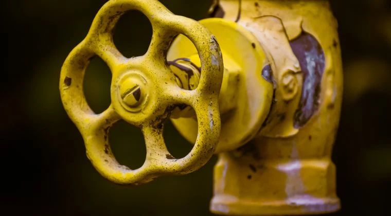 Close-up view of a rusty yellow shut-off valve, emphasizing industrial wear
