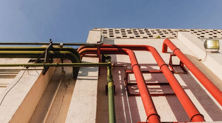 Close-up of vibrant red and green pipes on a sunlit urban building wall