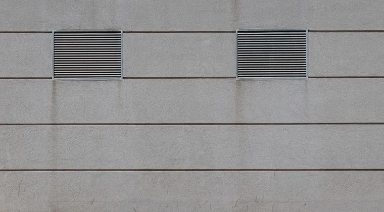 Minimalist concrete facade with two rectangular air vents in urban setting