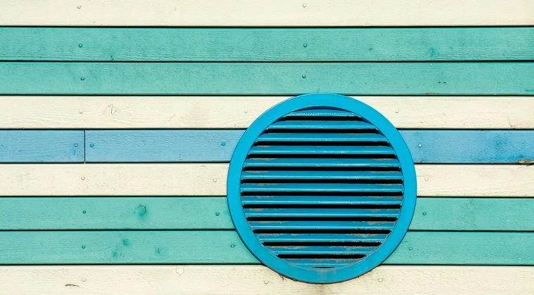 Vibrant blue, green, and cream striped wooden wall with a circular vent