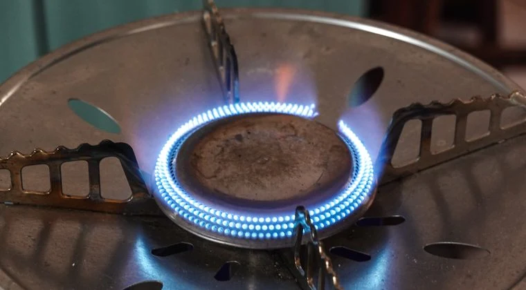 A detailed view of a lit gas stove burner with visible blue flames and metal support