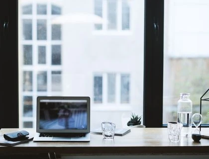 Sleek office desk setup featuring a laptop, glass of water, and open window view